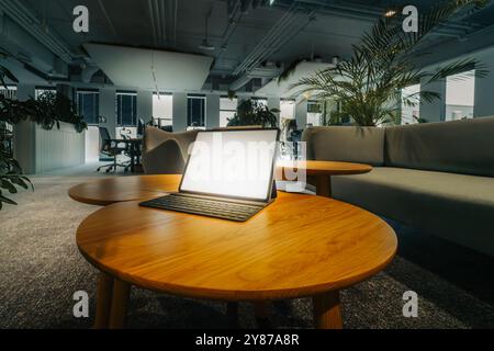 Laptop graphic tablet blank white glow screen on wooden table. Office space corporate interior. Industrial design green plants sofa. Stock Photo