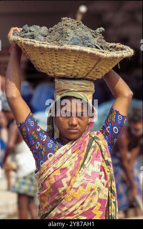 Bangladesh, Dhaka, young woman carries a basket of cement on a construction site. Stock Photo