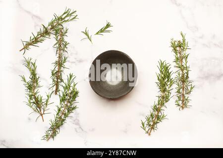 Branches of rosemary and an empty  bowl on a white marble kitchen countertop with copy space Stock Photo