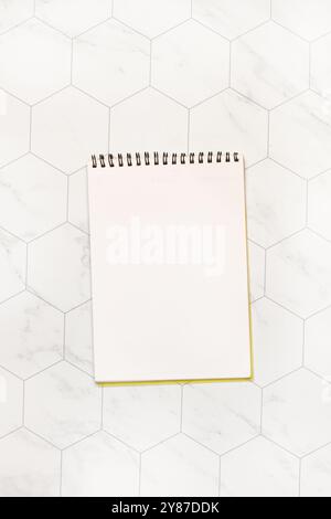 A spiral notepad open on a white page on a hexagonal tiled background Stock Photo