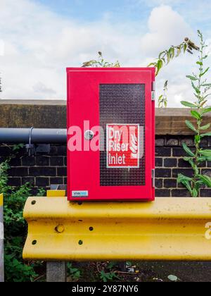 Manchester, UK, September 28, 2024: Red dry riser inlet on a yellow safety rail with plants and bricks in the background. Stock Photo