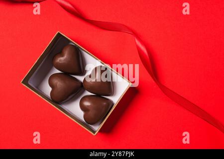 Heart shaped chocolate candies in a gift box on red background, top view. Valentine's day celebration Stock Photo