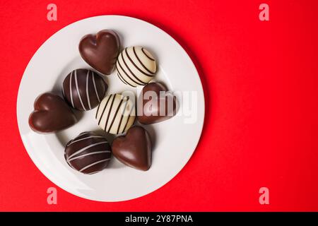 Delicious assorted chocolates on a white plate against a vibrant red background for Valentine's day celebration Stock Photo