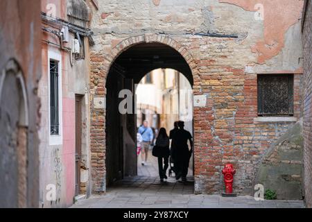 Street with archway in the historical italian town, Venice. Narrow alley in Venice with an old, weathered brick archway leading to another passageway. Stock Photo