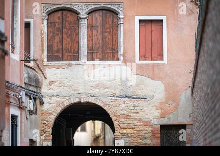 Street with archway in the historical italian town, Venice. Close-up of windows in historical house with brown blinds closed. Stock Photo