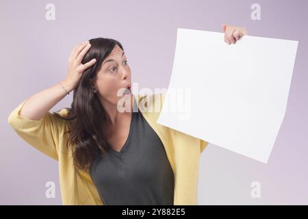 Woman holds a blank poster and looks at it with a surprised face, holding her hands to her head. Concept of sales and offers in business. Stock Photo