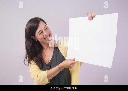 Woman looks smiling at the blank poster she holds in her hands. Image for business marketing. Stock Photo