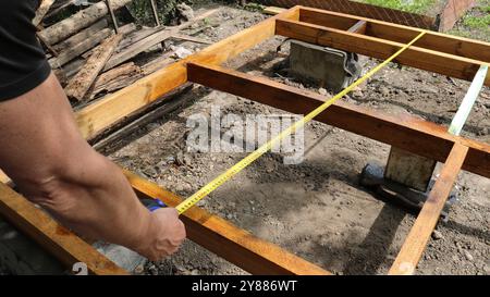 Frame worker holds tape measure against wooden post while working on ...