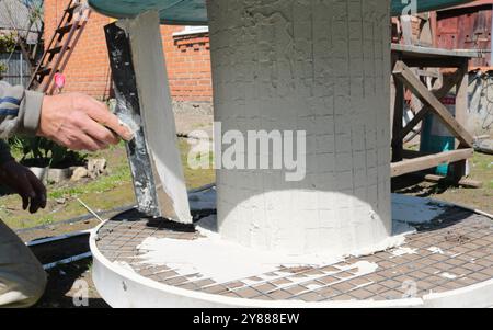 hands with a wide spatula coat the round leg of an outdoor table with mastic, applying a layer of mortar to furniture made by hand Stock Photo