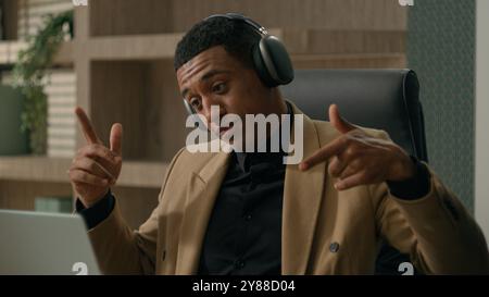 Carefree joyful African American happy business man listen music in headphones relax at workplace dancing businessman listening song in earphones Stock Photo