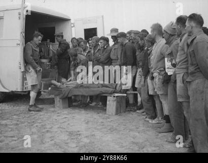 The answer to an urgent call in the desert for blood donors. As casualties come back to the dressing stations after heavy fighting in the Libyan offensive, one medical unit found itself in immediate need of more blood for transfusion purposes. There was a Royal Australian Air Force squadron nearby. A call for their help was made, and every man in the required blood group volunteered as a donor. This picture shows the line-up of airmen volunteers. Most of them had come straight from their work of servicing fighter aircraft. January 29, 1942. (Photo by A.I.F. Photography). Stock Photo