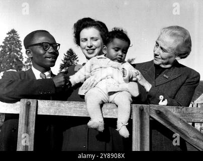 Lady Isobel's Farewell To Her Grandson -- Six-months-old Kwame Appiah he is with his parents Mr. and Mrs. Joseph Appiah, and his grandmother, Lady Isobel Cripps wore warm woollies when this picture was taken yesterday in Lady Isobel's garden at Oakbridge, near stroud, glos.But on Thursday, with his mother, Peggy, daughter of the late sir Stafford Cripps, Kwame sails for the gold coast, west Africa. And there, in his father's native Kumasi, Kwame won't need thick woollies. His mother says: 'He will wear nothing except his nappie and perhaps a little pair of pants on special occasions.' Mr. Appi Stock Photo