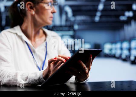 Trained serviceman using tablet to assess server security blips arising due to unsecured network connections. Qualified repairman ensuring data center is impenetrable by malware attacks Stock Photo