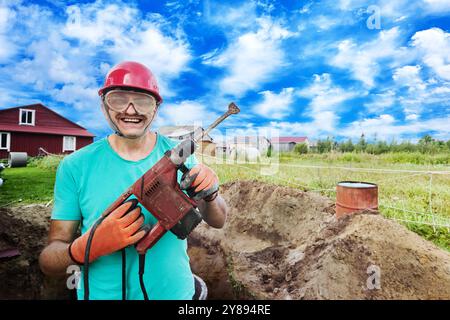 Satisfied builder in construction helmet and safety glasses holds hammer drill with chisel attachment in his hands. Stock Photo