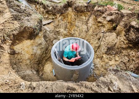 Septic tank builder crushes wall of concrete ring with drill with cord during installation of an autonomous sewage system in private country house. Stock Photo