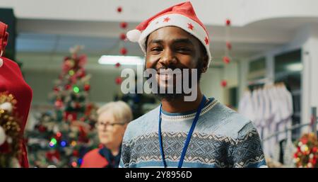 Portrait of smiling employee in Christmas decorated clothing store arranging neckties. Cheerful fashion shop worker preparing merchandise for holiday season shopping frenzy Stock Photo