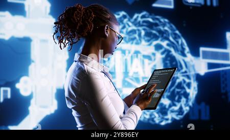 IT specialist updating AI systems, writing intricate binary code scripts on tablet, visualizing result wth AR. Licensed employee using programming to upgrade artificial intelligence simulation model Stock Photo