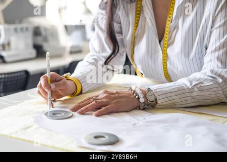 Beautiful young woman plus size dressmaker lays out pattern details on denim and cuts clothes Stock Photo