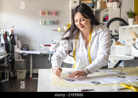 Beautiful young woman plus size dressmaker lays out pattern details on denim and cuts clothes Stock Photo