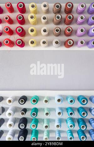 Multi-colored threads in spools and bobbins for sewing in a sewing workshop on a vertical Stock Photo