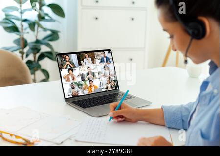 Side view of caucasian business woman having online meeting with her multiracial colleagues, talking about project plan and strategy via video conference, share ideas, takes notes Stock Photo