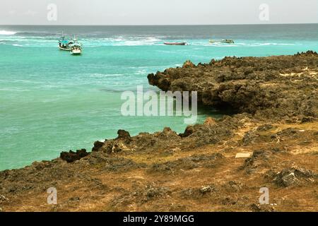 Rocky beach in a background of fishing boats on the coastal water of Pero in Pero Batang, Kodi, Southwest Sumba, East Nusa Tenggara, Indonesia. Stock Photo