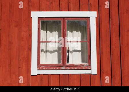 A red  wooden wall with an old window with curtain. Stock Photo