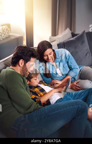 Parents, boy child and tablet on sofa in house for educational games, watching cartoon and bonding. Relax, people and family with digital app on couch Stock Photo