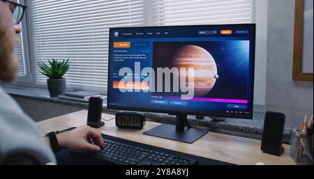 Adult man types prompt in AI video generator app on computer. PC screen shows artificial intelligence chatbot generating detailed high-quality video of Jupiter and its moon. Automated artwork concept. Stock Photo