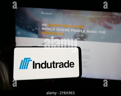 Person holding smartphone with logo of Swedish industrial company Indutrade AB on screen in front of website. Focus on phone display. Stock Photo