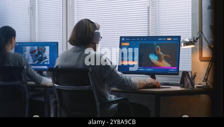Back view: Two diverse workers using AI generator on computers in office. PC screens showing artificial intelligence chatbot generating text prompt to realistic photo or video content. Generative art. Stock Photo