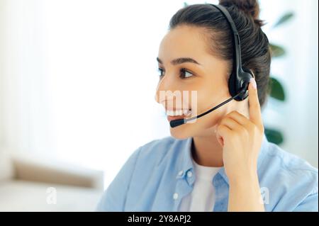 Side view close-up photo of a positive successful brunette caucasian woman with headset, working as call center operator, customer support service, hotline assistant, smiles while listening a client Stock Photo