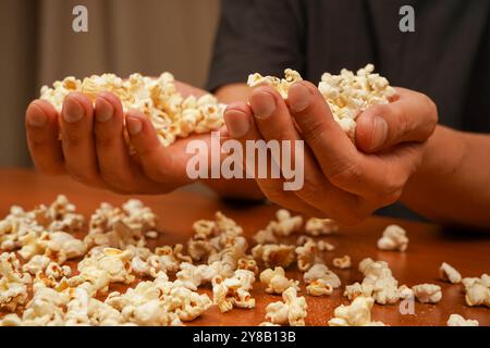 Popcorn scattered on table surface. Delicious snack to eat in the cinema. Flavored spicy popcorn in man's hands. Salted popcorn. Popcorn. Fast food Stock Photo