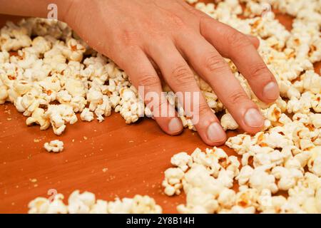 Snack for cinema. Popcorn scattered on table surface. Delicious snack to eat in the cinema. Flavored spicy popcorn in man's hands. Salted popcorn Stock Photo