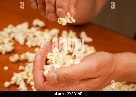 Popcorn scattered on table surface. Delicious snack to eat in the cinema. Flavored spicy popcorn in man's hands. Salted popcorn. Popcorn. Fast food Stock Photo