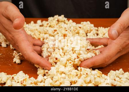 Flavored spicy popcorn in man's hands. Salted popcorn. Popcorn. Fast food. Junk food. Snack for cinema. Popcorn scattered on table surface. Delicious Stock Photo