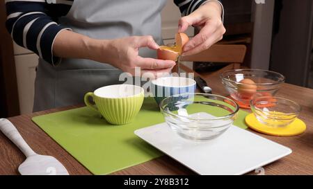 Process of making dough. Woman separates egg white from yolk in kitchen. Scales and eggs, utensils on wooden table. Baking macarons at home. Hands in Stock Photo