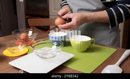 Process of making dough. Woman separates egg white from yolk in kitchen. Scales and eggs, utensils on wooden table. Baking macarons at home. Hands in Stock Photo