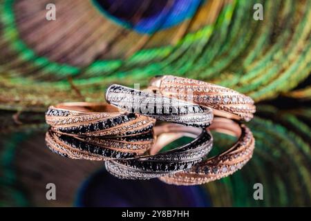 Wedding rings are reflected in the mirror. A set of three rings on a background of peacock feathers. Gold and silver rings with black and white stones Stock Photo