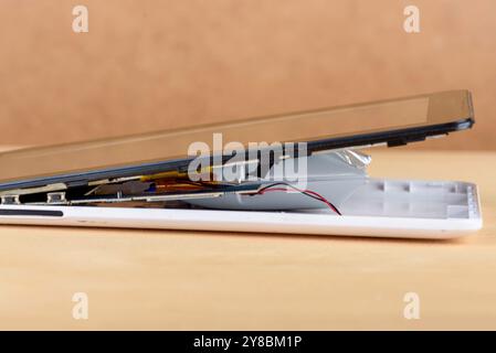 A close-up of a damaged smartphone revealing its internal parts and battery, on a neutral background Stock Photo