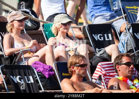 FANS IN DECKCHAIRS, BEACH VOLLEYBALL, MARIEHAMN, 2011: Two women in bikini tops and combat caps soak up the sport in the sunshine. People watch the beach volleyball action in relaxing deckchairs on the outer courts in summer clothing or beachwear on an unusually hot Baltic Sea summer day in August 2011 at the Paf Open in Mariehamn, Åland, Finland. Photograph: Rob Watkins.   INFO: Between 2009-2013 the PAF Open Beach Volleyball tournament was an annual event held in Mariehamn, Åland, Finland. It attracted the top international teams and players as a ranking part of the official FIVB World Tour, Stock Photo