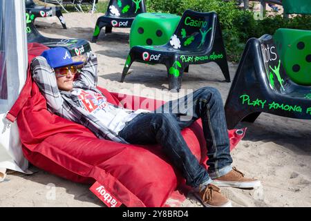 COOL GAMER LOOKING GUY CRASHED OUT, BEACH VOLLEYBALL, MARIEHAMN, 2011: A cool gamer looking guy in shades and a cap crashed out on an inflatable beach chair in August 2011 at the Paf Open in Mariehamn, Åland, Finland. Photograph: Rob Watkins.   INFO: Between 2009-2013 the PAF Open Beach Volleyball tournament was an annual event held in Mariehamn, Åland, Finland. It attracted the top international teams and players as a ranking part of the official FIVB World Tour, showcasing high-level beach volleyball. Stock Photo