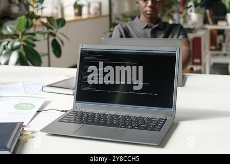 Medium close up of silver laptop with codes on black screen in modern office Stock Photo