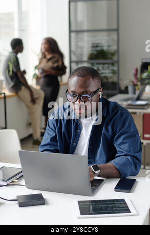Vertical shot of African American man sitting at work desk and typing on keyboard while listening to music Stock Photo