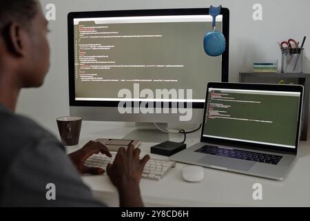 Unrecognizable talented programmer surrounded with electronic devices writing codes Stock Photo