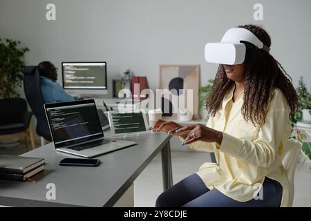 African American office worker with VR headset sitting at table and imitating typing on invisible keyboard Stock Photo