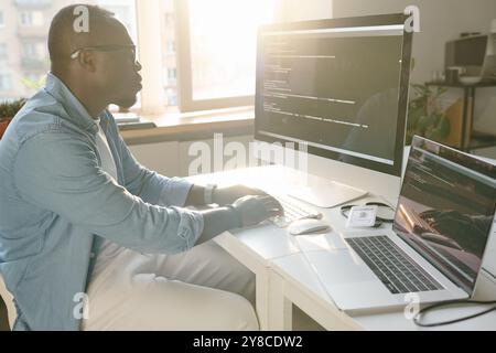 Side view shot of African American developer sitting at table and coding Stock Photo