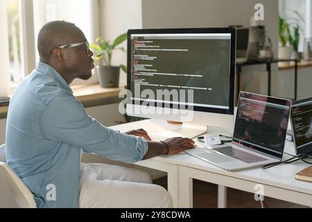 African American man sitting at table and coding in modern office Stock Photo