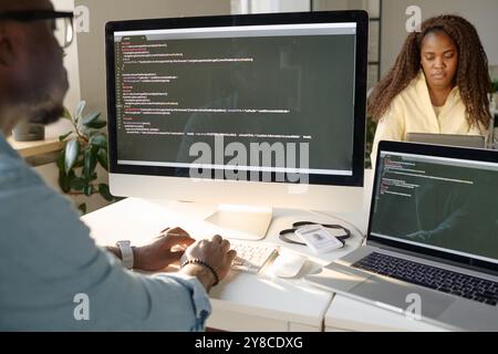 Unrecognizable man sitting at table and looking at computer screen while coding Stock Photo