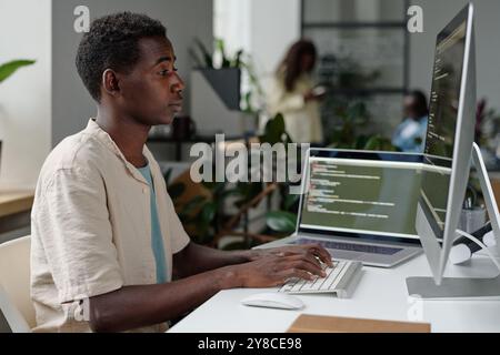 Tired African American programmer coding in cozy office full of plants and electronic devices Stock Photo